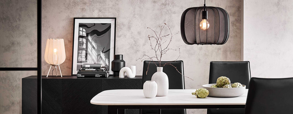 Modernes Esszimmer mit schwarzer Hängeleuchte aus Metallgeflecht, weißem Marmortisch, auf dem weiße vasen stehen, und schwarzem Sideboard im Industrial-Stil.