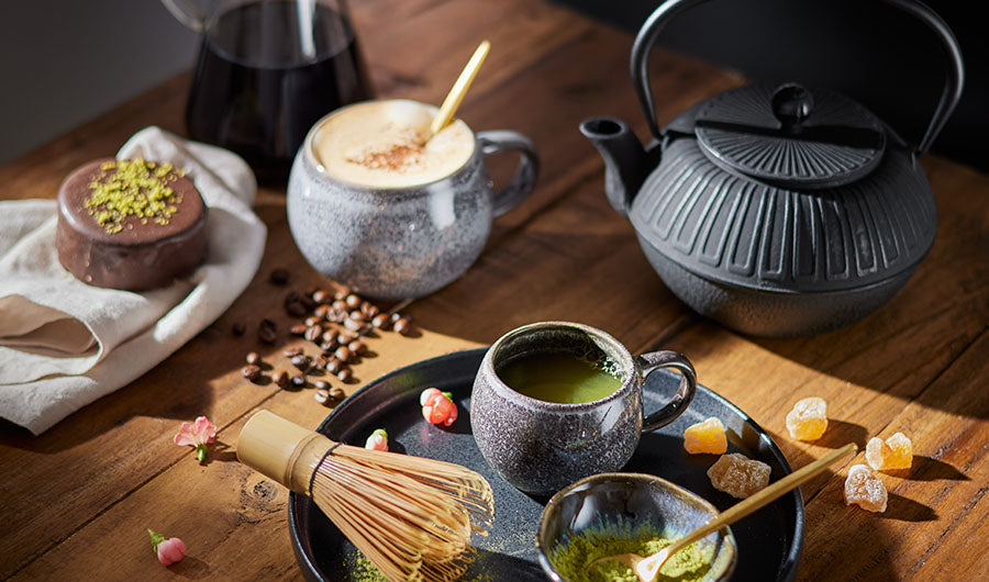 Matcha-Tasse und Kaffeebohnen neben schwarzer Teekanne auf Holztisch