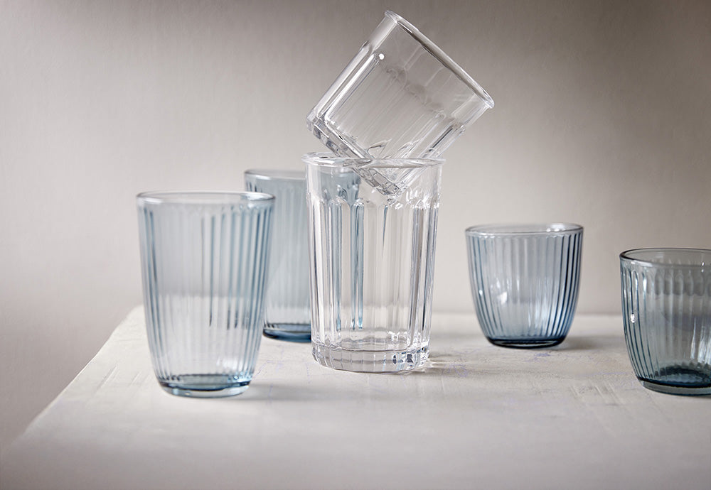 Set aus Trinkgläsern mit Rillenstruktur in transparent und Hellblau, stapelbare Wassergläser aus Glas auf einem weißen Tisch.