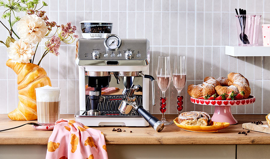 Espressomaschine auf Küchentheke mit Latte Macchiato und Croissants