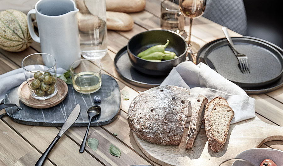 Gedeckter Holztisch im Freien mit frischem Brot und Besteck