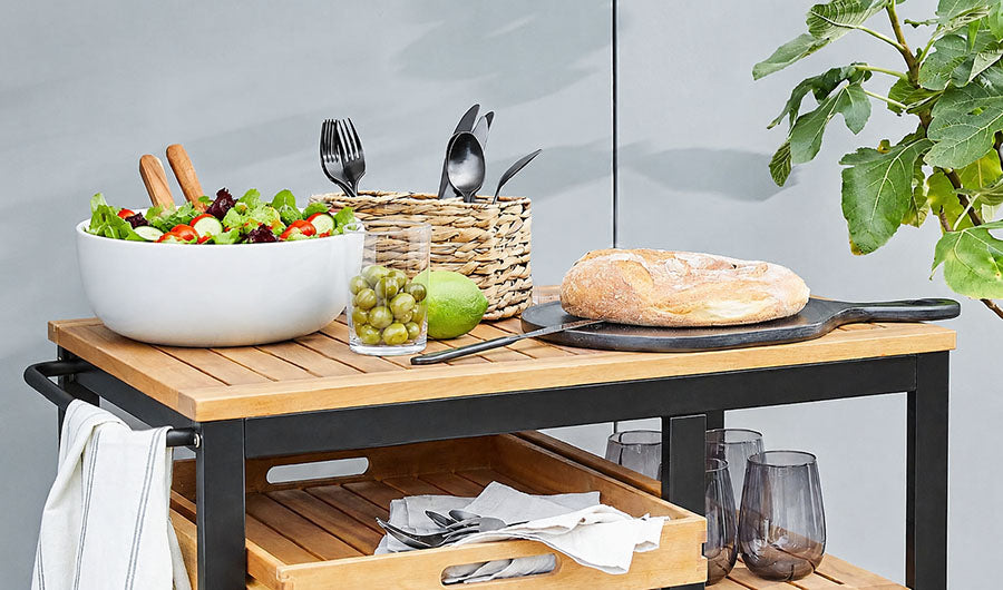 Weiße Salatschüssel mit frischem Salat auf Teak-Servierwagen im Freien