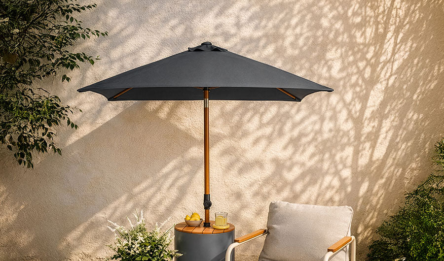 Dunkelgrauer Sonnenschirm mit Holzmast auf heller Terrasse mit Sessel