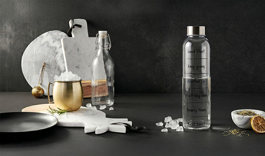 Glastrinkflasche mit Motivations-Markierungen neben goldenem Becher auf Dunkelgrau