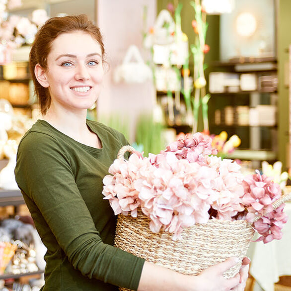 Lächelnde Mitarbeiterin mit Korb voll rosa Blüten im Store
