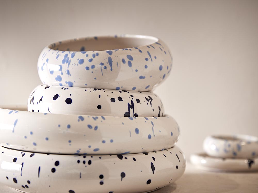 Stapel aus weißen Keramikschalen Boogy Splash mit blauen Farbspritzern als dekorative Statement-Pieces für den gedeckten Tisch.