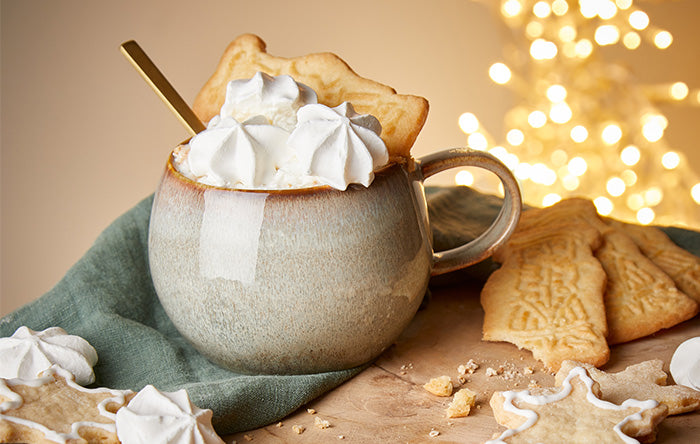 Reaktivglasierter Becher mit Sahne und Gebäck vor Lichterkette