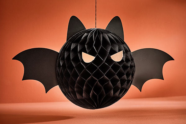 Schwarze, kugelförmige Fledermaus-Dekoration mit Flügeln und leuchtenden Augen vor orangefarbenem Hintergrund.