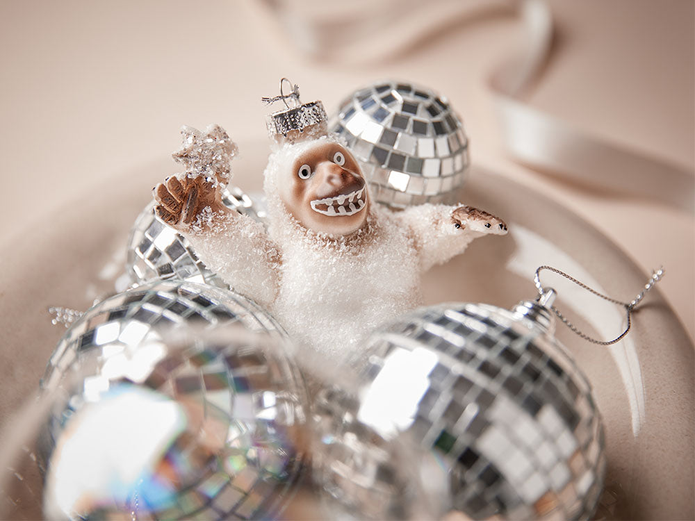 Yeti-Baumanhänger zwischen silbernen Discokugel-Weihnachtskugeln