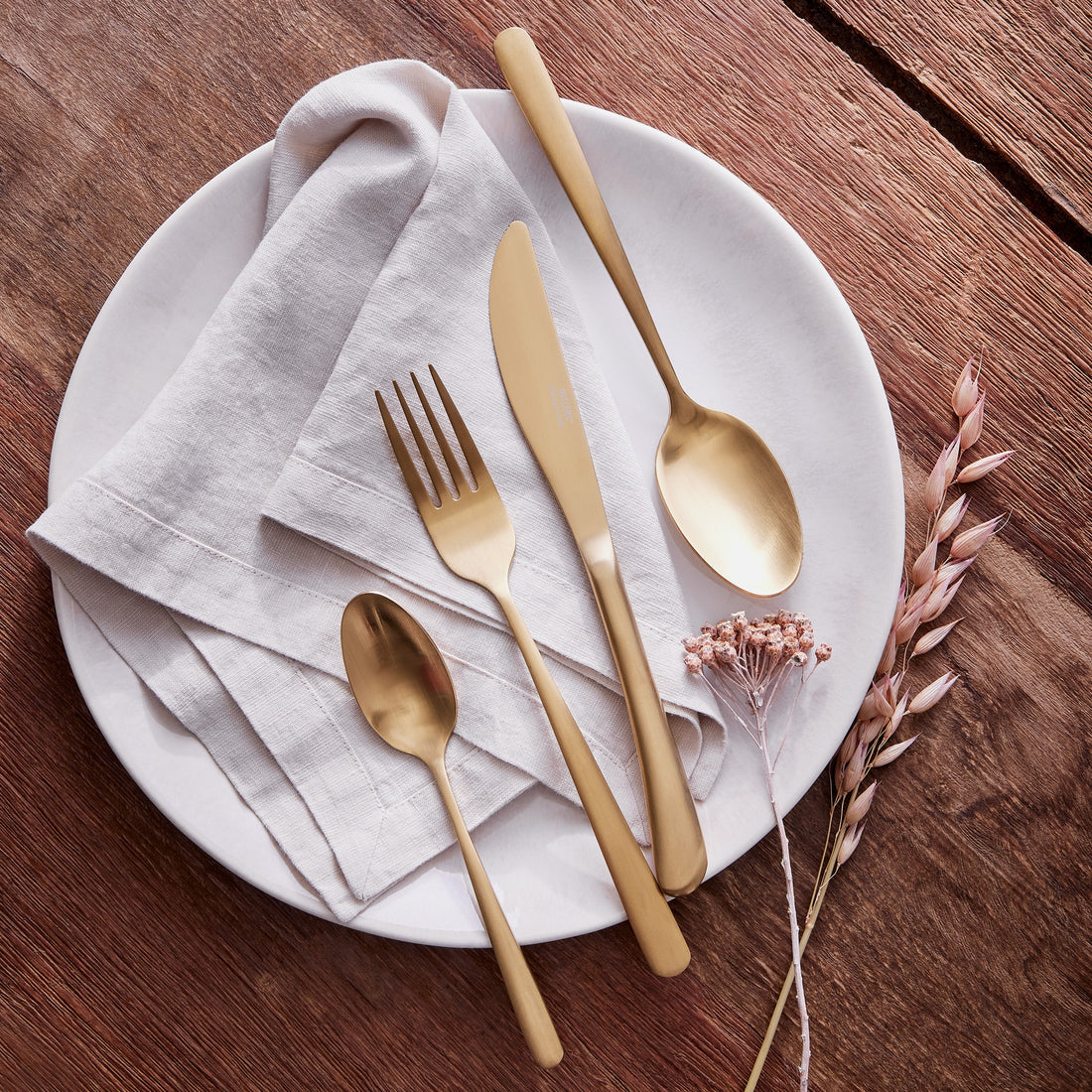 Mattgoldenes Besteck-Set aus Edelstahl auf einer hellen Leinenserviette und einem weißen Keramikteller im eleganten Vintage-Stil.