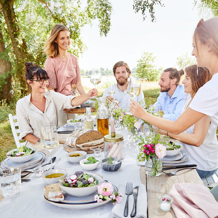 Freunde feiern sommerliches Gartenessen an gedecktem Tisch am See