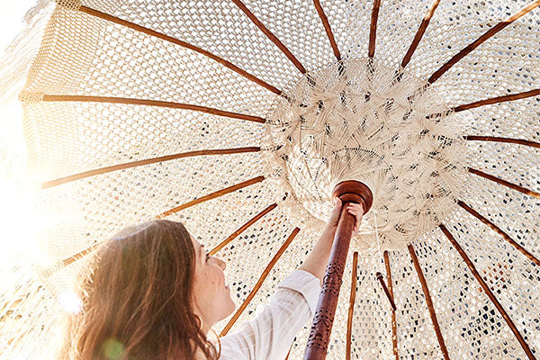 Nahaufnahme eines hellen Sonnenschirms aus Makramee-Gewebe mit Holzstreben und handgefertigten Details im Boho-Stil.