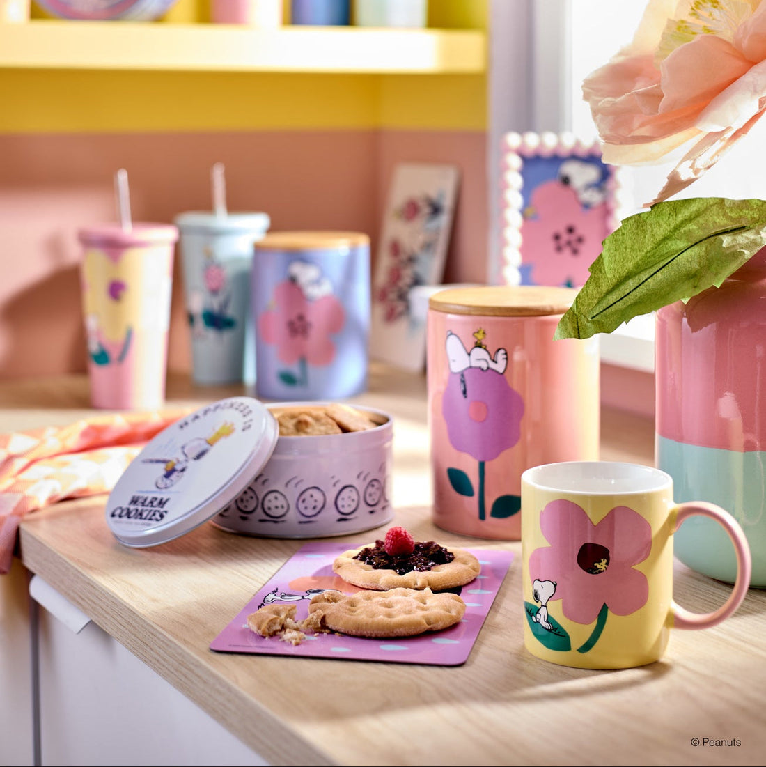 Peanuts Frühstücks-Set aus Keramik mit Snoopy-Motiv, bestehend aus gelber Tasse, rosa Vorratsdose und Keks-Dose auf einer hellen Holzküche.
