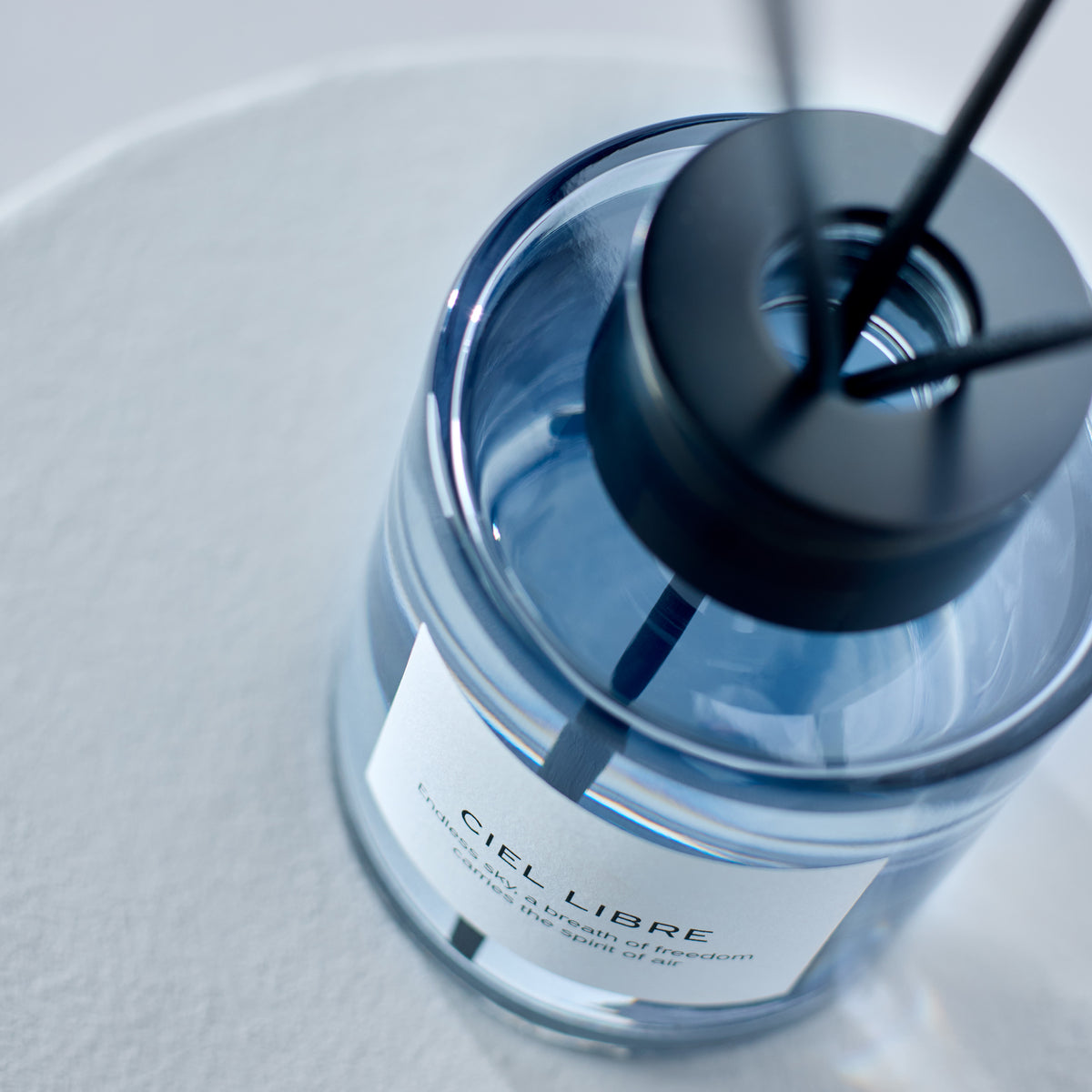 Detailansicht eines Ciel Libre Raumduft-Flakons aus blauem Glas mit schwarzem Verschluss und Diffuser-Stäbchen für modernes Interior Design.