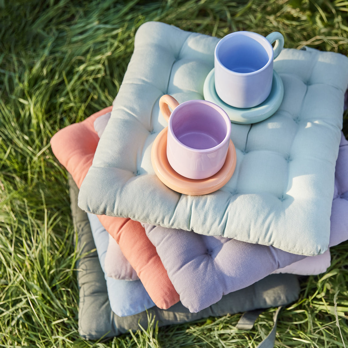 Bunte quadratische Outdoor Sitzkissen auf Baumwolle mit zwei Tassen oben drauf.