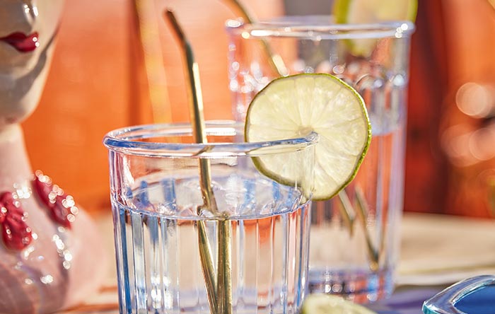 Zwei transparente Wassergläser mit Reliefmuster und goldenen Trinkhalmen, dekoriert mit einer Limettenscheibe.